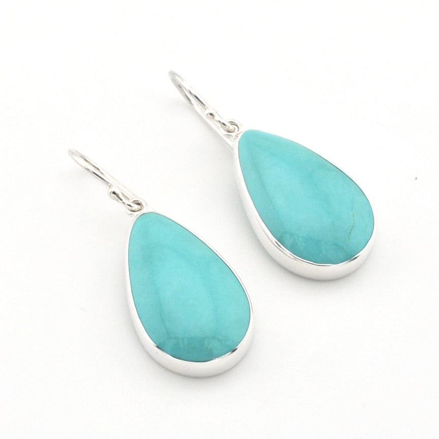 A pair of silver drop earrings featuring teardrop-shaped turquoise gemstones, displayed on a clean white background.