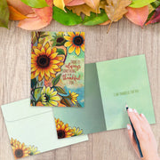 Greeting card with sunflowers and a motivational quote on a wooden surface with autumn leaves.