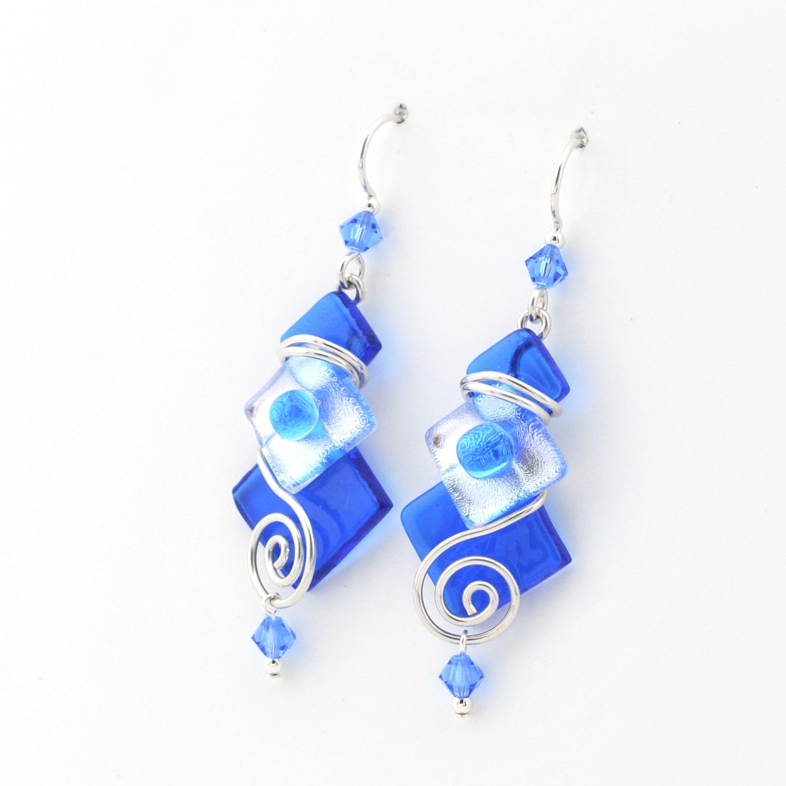 Blue glass earrings with silver swirl designs on a white background