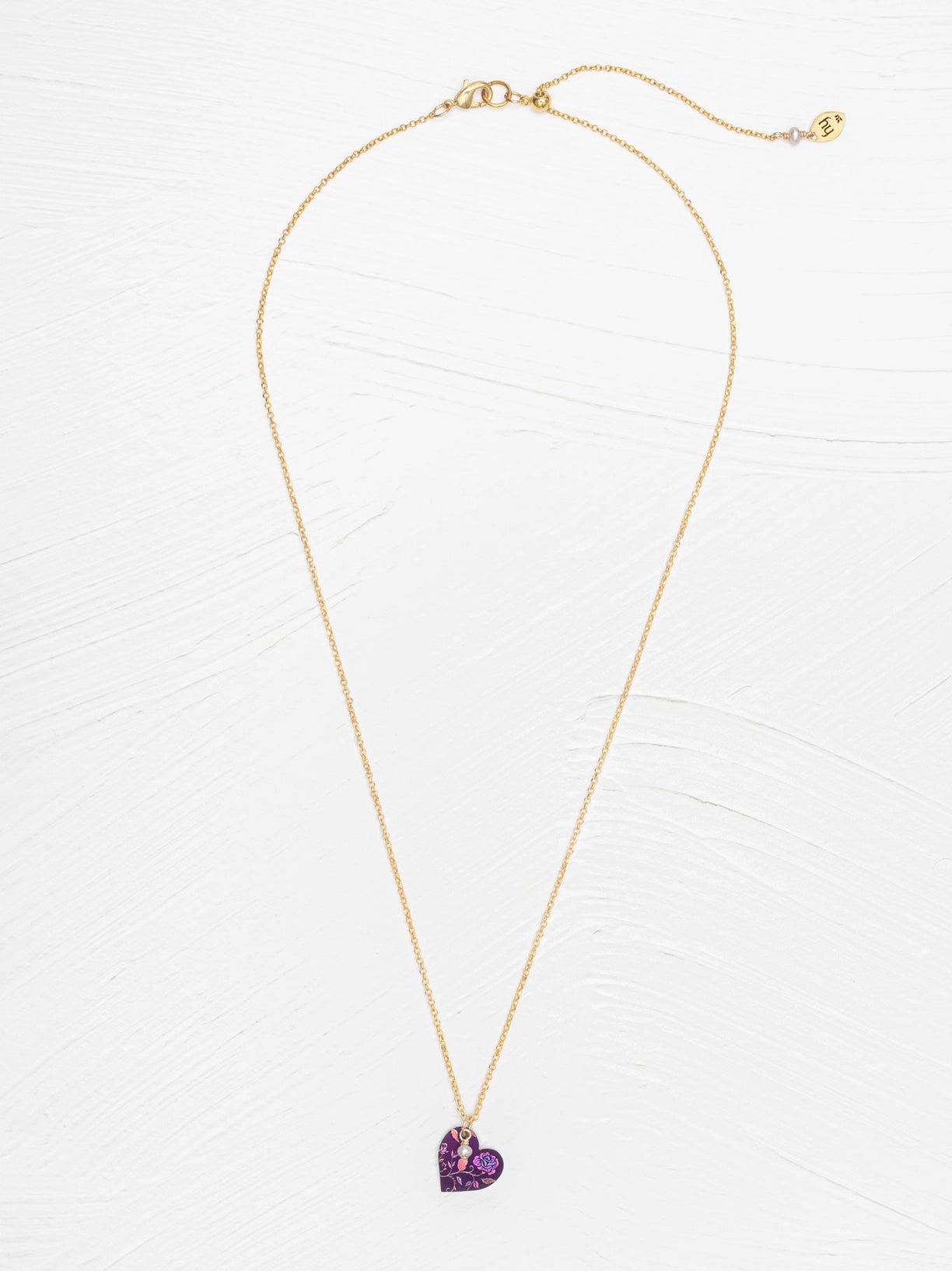 Gold necklace with a purple heart-shaped pendant on a white background