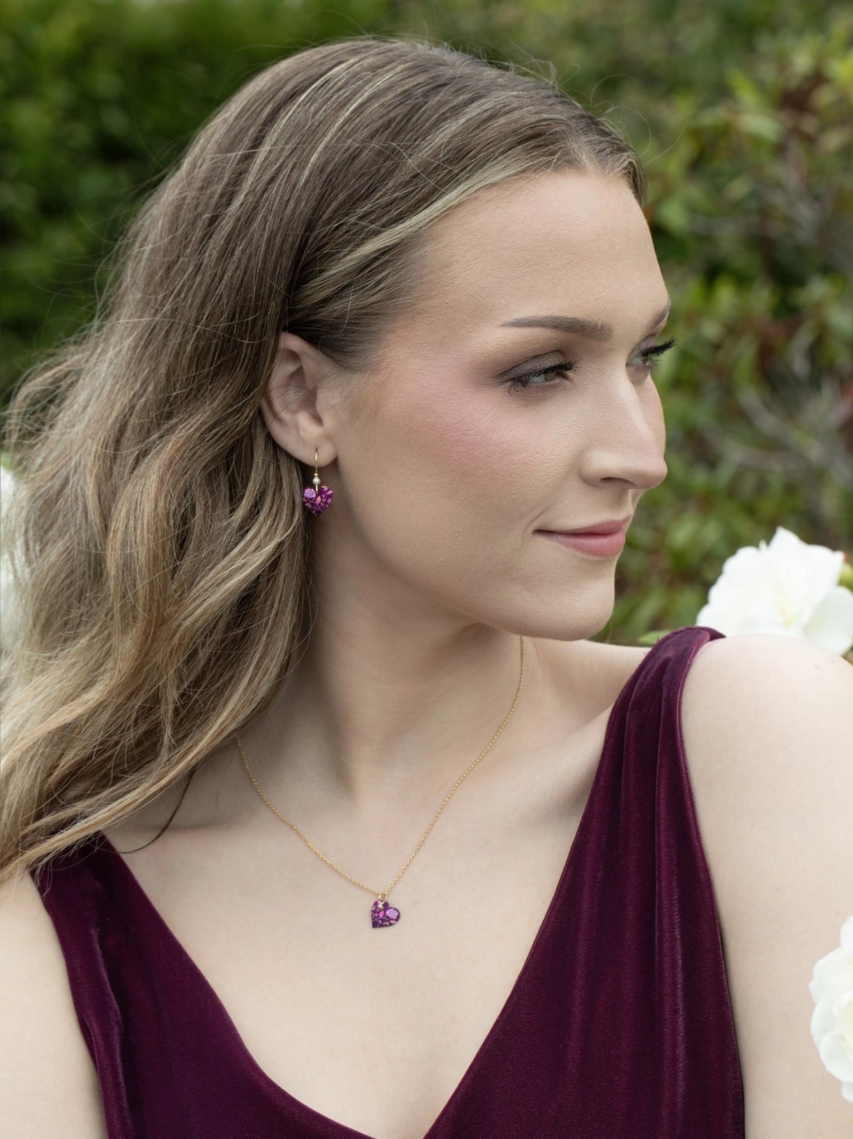 Woman wearing a purple dress with a necklace and earrings, standing outdoors.