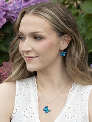 Woman wearing blue butterfly earrings and necklace with a floral background